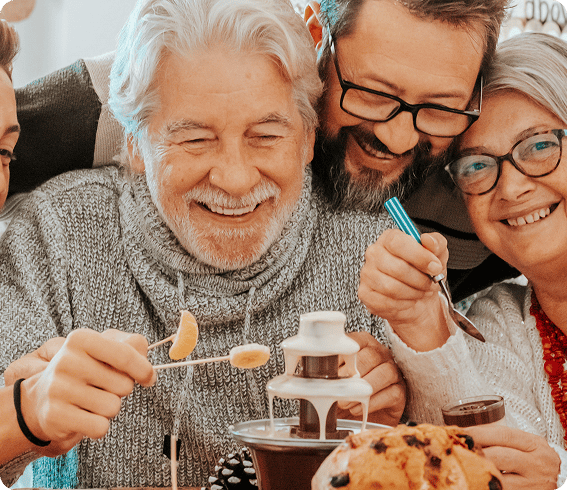 Smiling elderly man missed AEP and has no medicare coverage, and two adults enjoying dipping fruit into a chocolate fountain together.