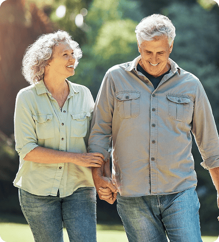 Smiling elderly couple from Philadelphia on medicare holding hands and walking outdoors in a sunny park.