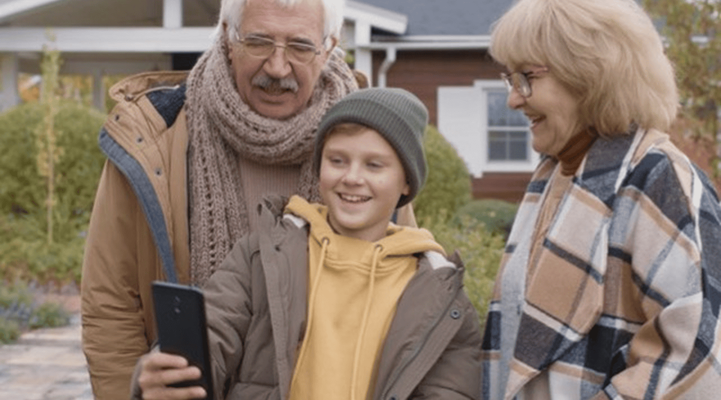 A smiling boy in Cleveland Ohio in a beanie and winter coat takes a selfie with happy elderly man on medicare and woman outdoors.
