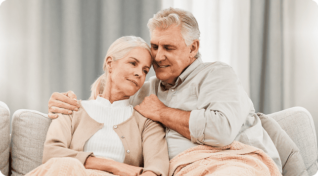 Senior couple with specialist physician paid for by medicare sitting on a couch, wrapped in blankets, sharing an affectionate moment.