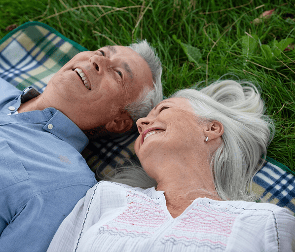 Smiling elderly couple missed enrollment deadline  lying on a blanket in green grass looking content.