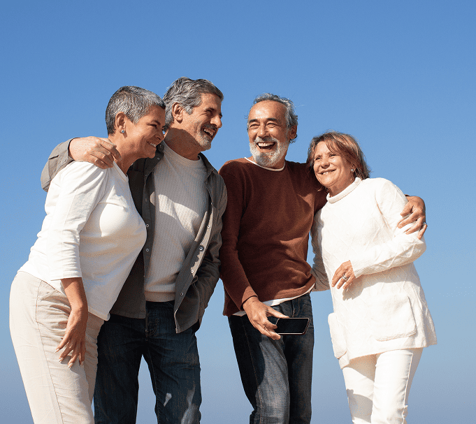 Four smiling older adults with great medicare coverage in pennsylvania standing closely together outdoors under a clear blue sky, embracing each other affectionately.